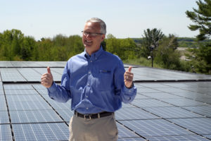 David Greer, with the rooftop solar system on his company, Wirebelt of America, says “I just love the stuff!” Image from Green Energy Times, December 2013.